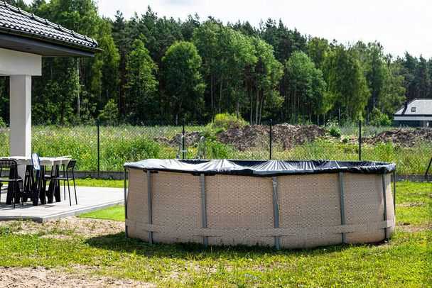 Large expansion pool with a diameter of 3.96 meters with black cover, set in the backyard next to the house. - Fotó, kép