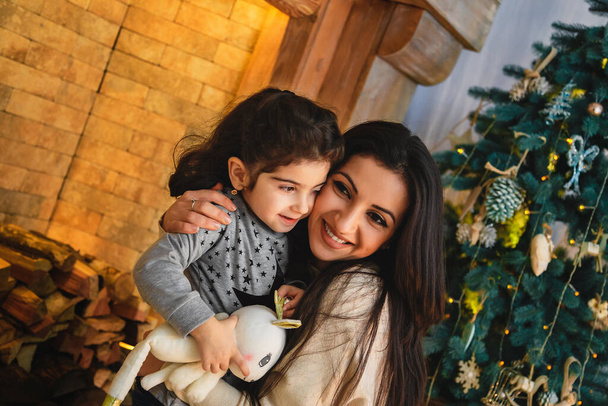 Vánoční rodinný portrét šťastně se usmívající matky objímající malou dceru poblíž vánočního stromečku. Zimní dovolená Vánoce a Nový rok koncept. - Fotografie, Obrázek