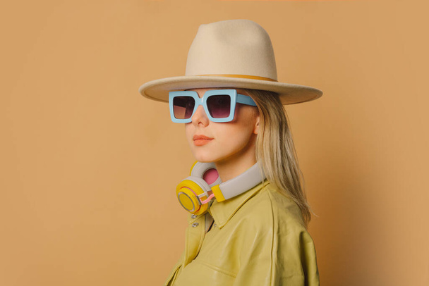 Stylish 80s woman in eyeglasses, headphones and hat on brown background - Foto, Imagen