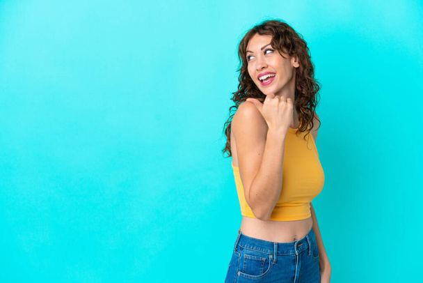 Young woman with curly hair isolated on blue background pointing to the side to present a product - Photo, Image