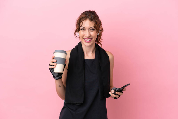 Sport sport woman with towel isolated on pink background holding coffee to take away and a mobile - Photo, Image