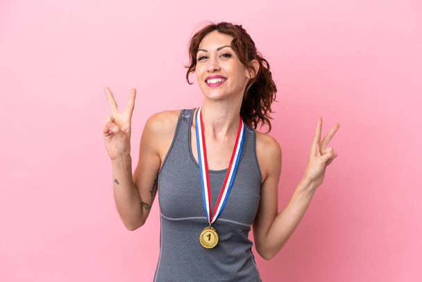 Young caucasian woman with medals isolated on pink background showing victory sign with both hands - Photo, image