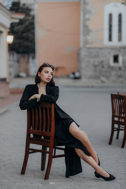 a brunette girl in a black jacket and dress and black glasses sits in a cafe - Valokuva, kuva