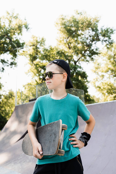 Happy young child boy with skate board on playground and smile. Extreme sport lifestyle. Smiling child with skate board posing on sport ramp - Foto, imagen