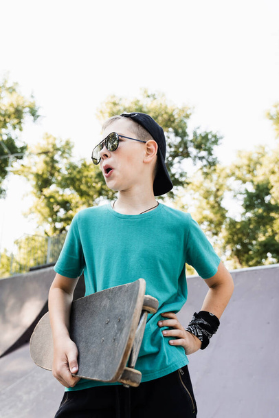 Fashion child boy in glasses posing with skate board on sport playground. Active teenager with sport equipment on sport ramp. Extreme lifestyle - Fotoğraf, Görsel