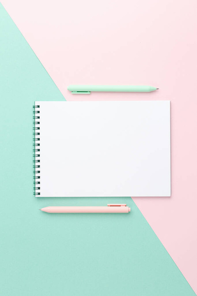 White sheet spiral notebook with a blue and pink pen on a two color background. Top view. Spring concept. - Foto, Bild
