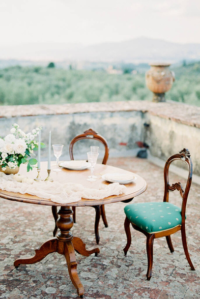 Zachte stoelen staan voor een gedekte feestelijke tafel met kaarsen en glazen. Hoge kwaliteit foto - Foto, afbeelding