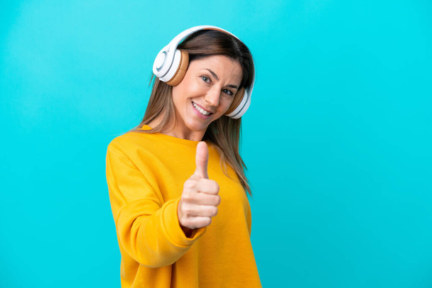Middle age caucasian woman isolated on blue background listening music and with thumb up - Foto, Imagen
