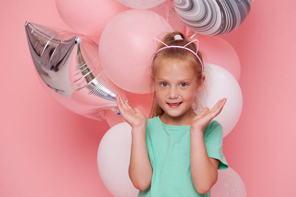 Joyful child girl in elegant tulle dress near the balloons. Birthday present. Funny face celebrates birthday party on pink background	 - Фото, изображение