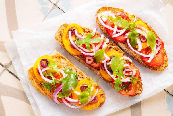 Healthy vegetarian toasts on parchment paper. Vegetarian sandwiches with fresh tomato, greens and olives. Vegetarian spanish tapas on til. Top view - Foto, Imagem
