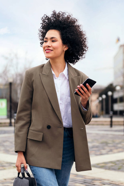 portrait of a smiling business woman walking with a smart phone in her hand, technology and communication concept - Photo, Image