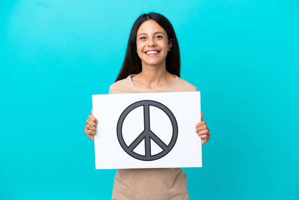 Mujer joven sobre fondo aislado sosteniendo un cartel con símbolo de paz con expresión feliz - Foto, imagen