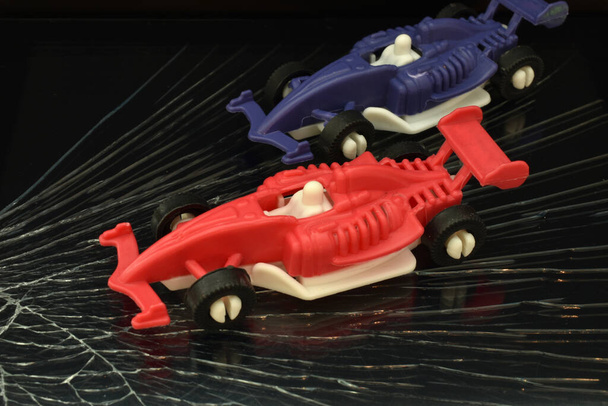 De foto toont kinderspeelgoed racewagens in rood en paars op een donkere weg. - Foto, afbeelding