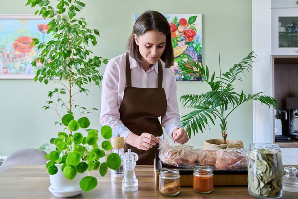 Young woman in apron cooking meat in roasting sleeve, using spices baking bag, kitchen at home. Holiday, traditional cuisine, cooking and eating at home concept - Photo, image