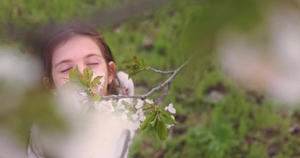 Niña oliendo el aroma de los árboles de primavera en flor en el huerto de manzanas. Mujer búlgara en vestido de folclore en el jardín - Imágenes, Vídeo