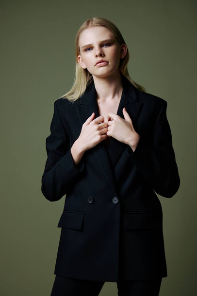 The model holds the jacket by the collar while posing on a green background in the studio. Concept photo for clothing brands. Cool offer for fashionable suits. High quality photo - Photo, Image