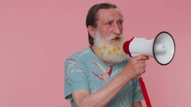 Happy bearded senior man talking with megaphone, proclaiming news, loudly announcing sale advertisement, warning using loudspeaker to shout speech. Elderly mature grandfather on pink studio background - Footage, Video