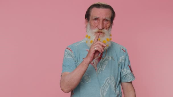 Shh be quiet please. Portrait of mature flowered beard man presses index finger to lips makes silence gesture sign do not tells secret. Elderly senior handsome grandfather on pink studio background - 映像、動画