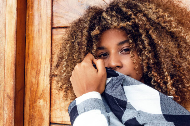 portrait of curly haired afro young teen woman in blue jacket covering her face in fashion on wooden background. - Foto, Bild
