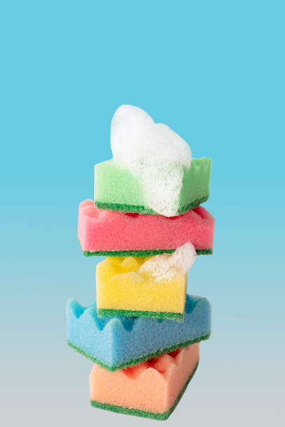 Pila di spugne colorate per la pulizia della cucina con bolle di sapone su sfondo blu. Vista frontale - Foto, immagini