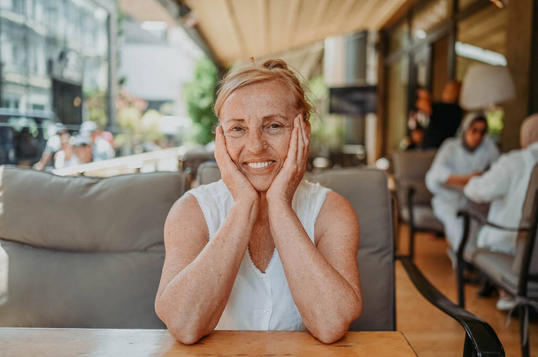 Happy senior woman with perfect smile and teeth sitting outdoors at summer sidewalk street cafe or restaurant terrace. Retired mature people holiday vacation, active lifestyle concept - Foto, Imagen