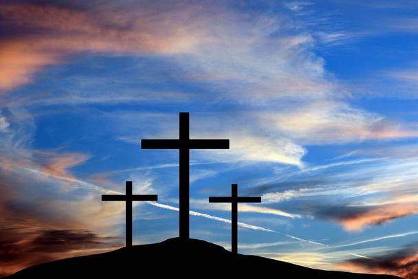 Die drei Kreuze der Kreuzigung Jesu Christi sind in dieser 3-D-Illustration in Silhouetten vor einem bunten Himmel zu sehen. - Foto, Bild