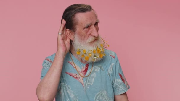 I cant hear you. What. Man trying hear you, looking confused and frowning, keeping arm near ear for louder voice, asking to repeat, to hear information, deafness. Senior grandfather on pink background - Materiał filmowy, wideo