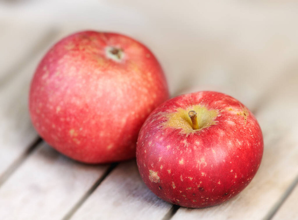 Два червоних яблука на дерев'яному столі в приміщенні. Їжте здорове і спостерігайте за своєю дієтою. Плоди містять необхідні вітаміни для підвищення вашого імунітету. Крупним планом смачні закуски веганів і вегетаріанців можуть насолоджуватися
. - Фото, зображення