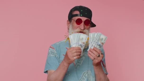 Rich pleased boss senior man waving money dollar cash banknotes bills like a fan, success business career, lottery winner, big income, wealth. Elderly grandfather isolated on pink studio background - Πλάνα, βίντεο