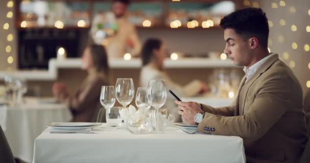 4k videokuvaa nuoresta miehestä, joka käyttää älypuhelintaan odottaessaan jotakuta ravintolassa. - Materiaali, video