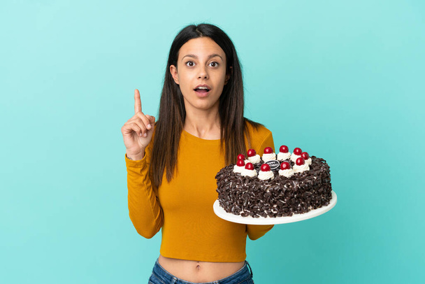 Young caucasian woman holding birthday cake isolated on blue background intending to realizes the solution while lifting a finger up - Foto, Imagen