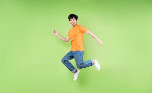 fiatal ázsiai férfi jumping, elszigetelt zöld háttér - Fotó, kép
