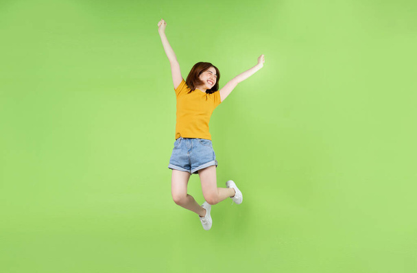 Jovem menina asiática pulando em um fundo verde - Foto, Imagem