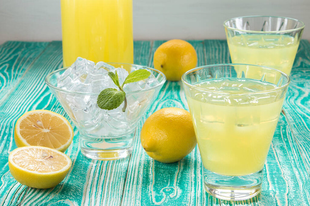 lemonade or limonchello in glasses glasses with ice cubes, sherbet glass with ice cubes decorated by mint leaf, lemon fruits on turquoise colored wooden table with yellow napkin at white polka dots - Foto, immagini