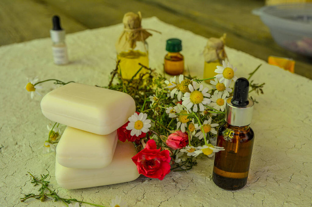 Bottle of chamomile essential oil and soap bars on light blue wooden table in field .Soap, antiseptic, medicinal chamomile flowers, aromatic oil for hygienic procedures - Photo, Image