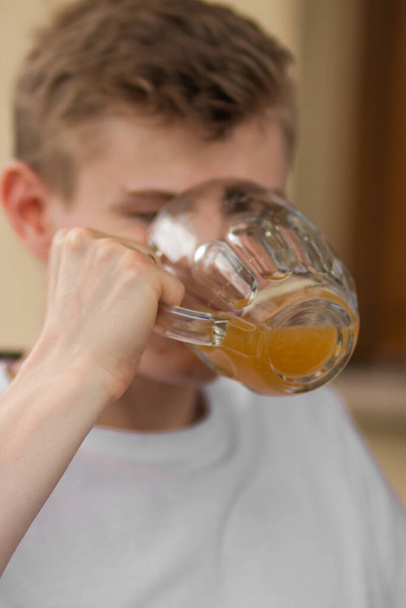 Caucasian young blond man in white t-shirt enjoying and drinking tasty beer in pub. Space for text. Unhealthy alcohol drink. Summer weekend with beer and friends. - Photo, Image