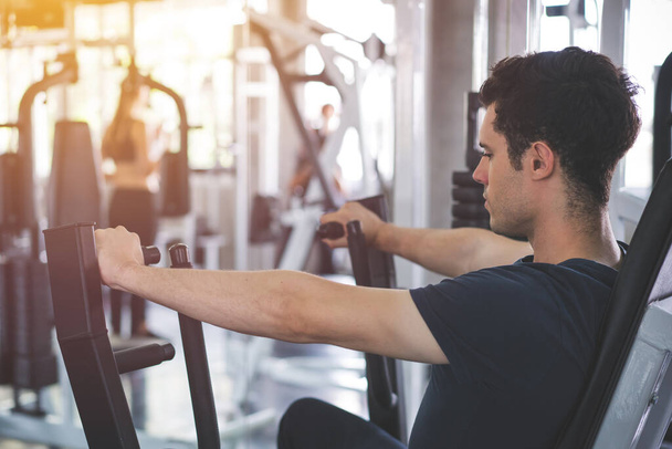 Jóképű férfi fogyás fitness gép és edzés az edzőteremben. - Fotó, kép