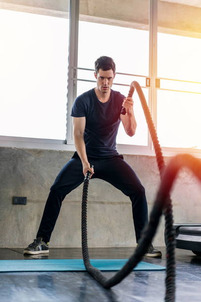 Handsome man doing battle ropes exercise workout it best cardio at fitness gym. - 写真・画像