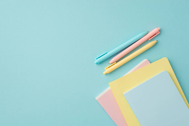 Okul malzemeleri konsepti. İzole edilmiş pastel mavi arkaplan üzerindeki renkli kırtasiye kalemlerinin ve kopya kitaplarının en üstteki görünümü - Fotoğraf, Görsel