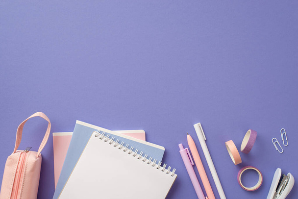 Back to school concept. Top view photo of notebooks pens adhesive tape stapler clips and pink pencil-case on isolated lilac background with copyspace - Photo, image