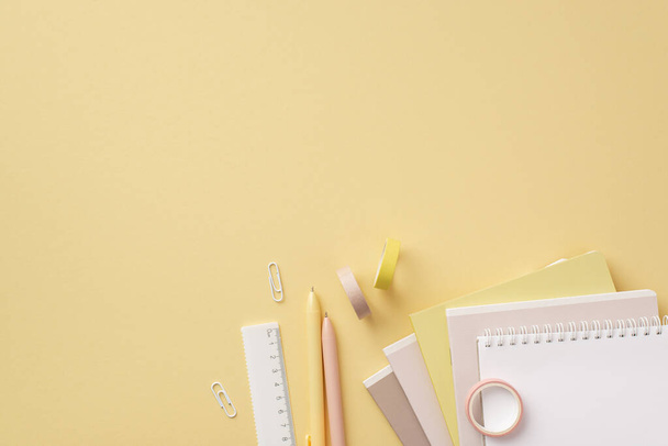 School accessories concept. Top view photo of stationery ruler clips stack of notebooks adhesive tape and pens on isolated pastel yellow background with copyspace - Zdjęcie, obraz