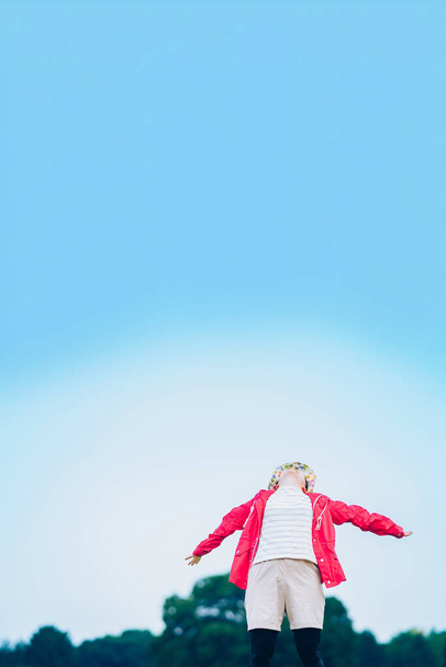 A woman taking a deep breath in the meadow under the blue sky - 写真・画像
