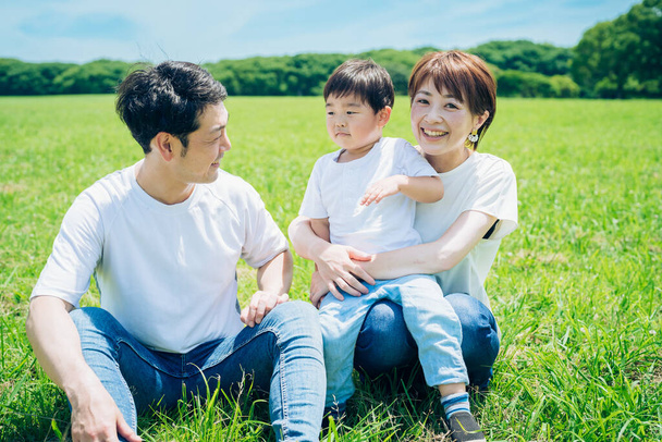 Parents and their child sitting on a sunny green space on fine day - Photo, image