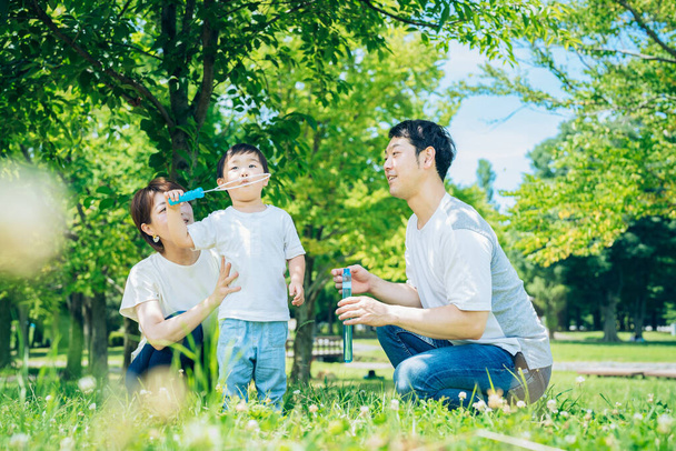 Parents and their child playing with soap bubbles at the park - 写真・画像