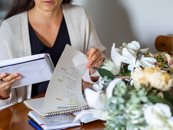 Freelance woman comparing documents and working from home. Checking goals and consulting papers for study and planning day. Entrepreneur in home office with notebook, flowers and paperwork. - Photo, image