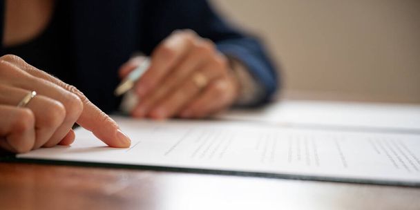 Lage hoek close-up zicht van zakenman of advocaat wijzend naar een handtekening lijn aan de onderkant van juridisch document of contract. - Foto, afbeelding