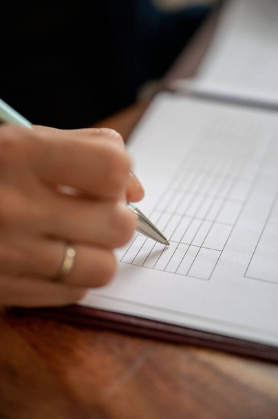 Крупный план заполнения деловой женщиной данных в таблице, напечатанной на белой бумаге. - Фото, изображение