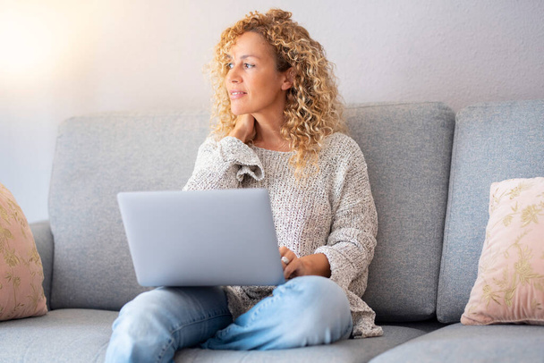 Serene single woman with laptop and internet connection at home. Female enjoy modern online working activity on computer. People and leisure indoor activity or alternative job office sitting on couch - 写真・画像