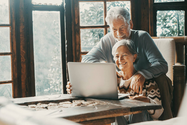 Old senior couple at home use laptop for video call to friends or parents. Distance and remote communication with laptop and internet technology. Elderly people enjoy day and lifestyle using notebook - Foto, Imagem