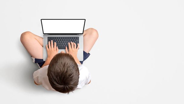 Boy sitting and working on a laptop. View from above. Isolated display for mockup, website promotion, app or game. Copy space beside - Fotoğraf, Görsel